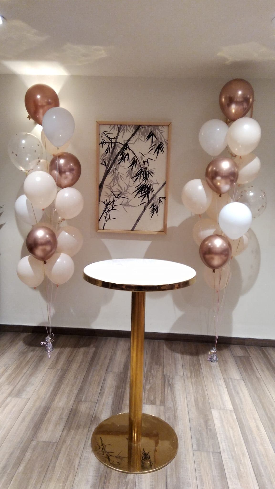 Rose gold and white helium balloon bouquets either side of a cocktail table