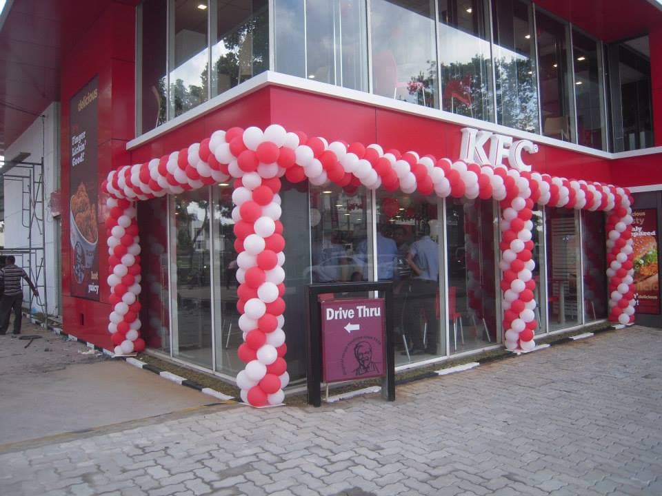 Red and white balloon columns and arch framing a KFC store entrance for its opening